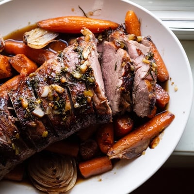 Roasted Lamb Leg with Rosemary and Garlic slices showcase tender, pink meat infused with aromatic herbs, served with roasted vegetables and a drizzle of sauce.