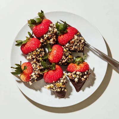 On a marble counter, chocolate dipped strawberries with nuts are arranged artfully, ideal for elegant dessert platters or romantic gifts.  