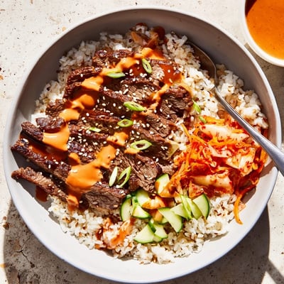 Korean BBQ steak rice bowls topped with crisp veggies and creamy Sriracha drizzle